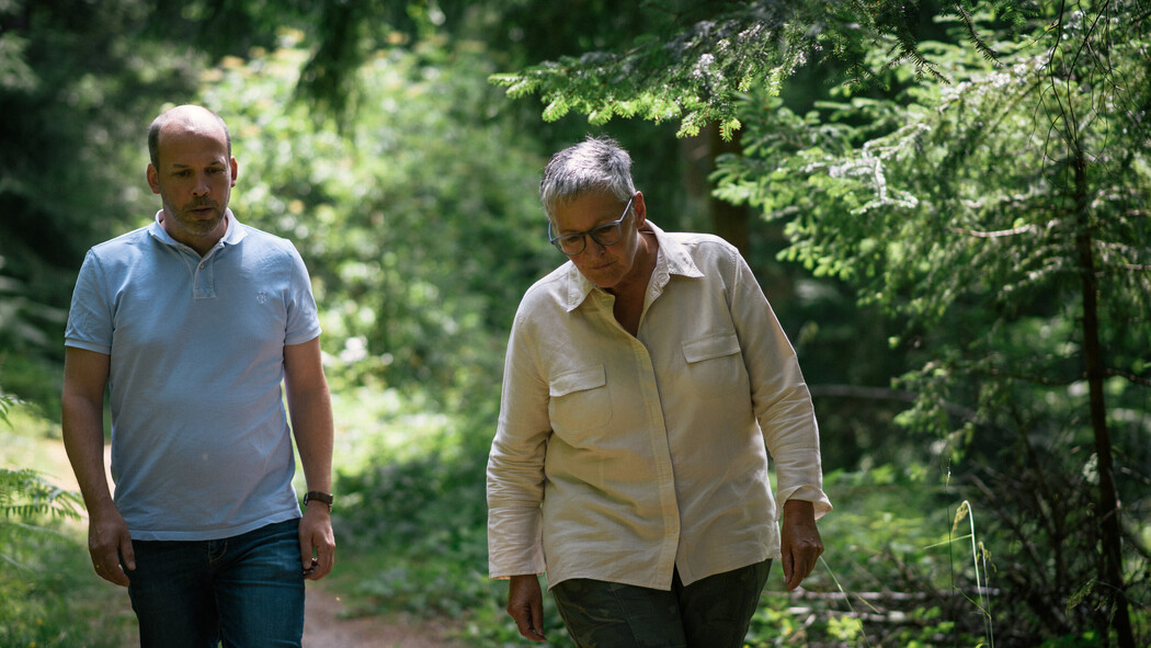 zwei personen spazieren im wald, mann tr&auml;gt blaues shirt und frau wei&szlig;e bluse